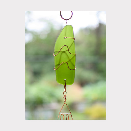 Green glass wind chime with copper wire design against a blurred natural background
