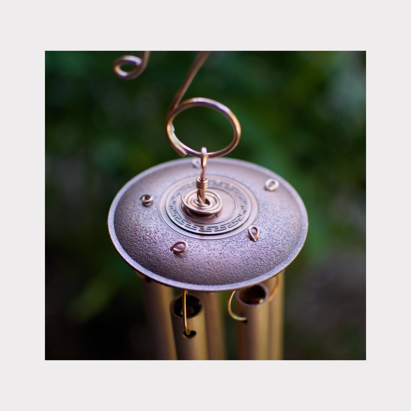 Close-up of a metallic wind chime with a blurred green background