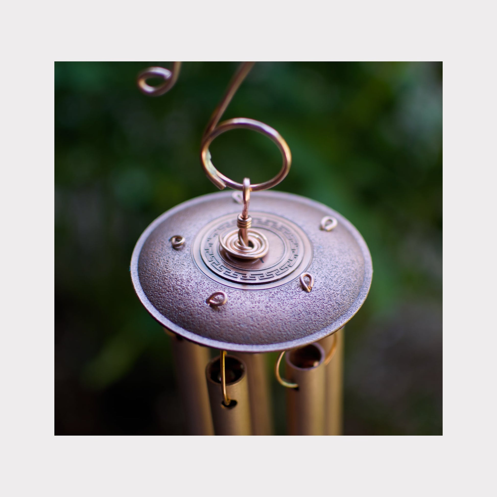 Close-up of a metallic wind chime with a blurred green background
