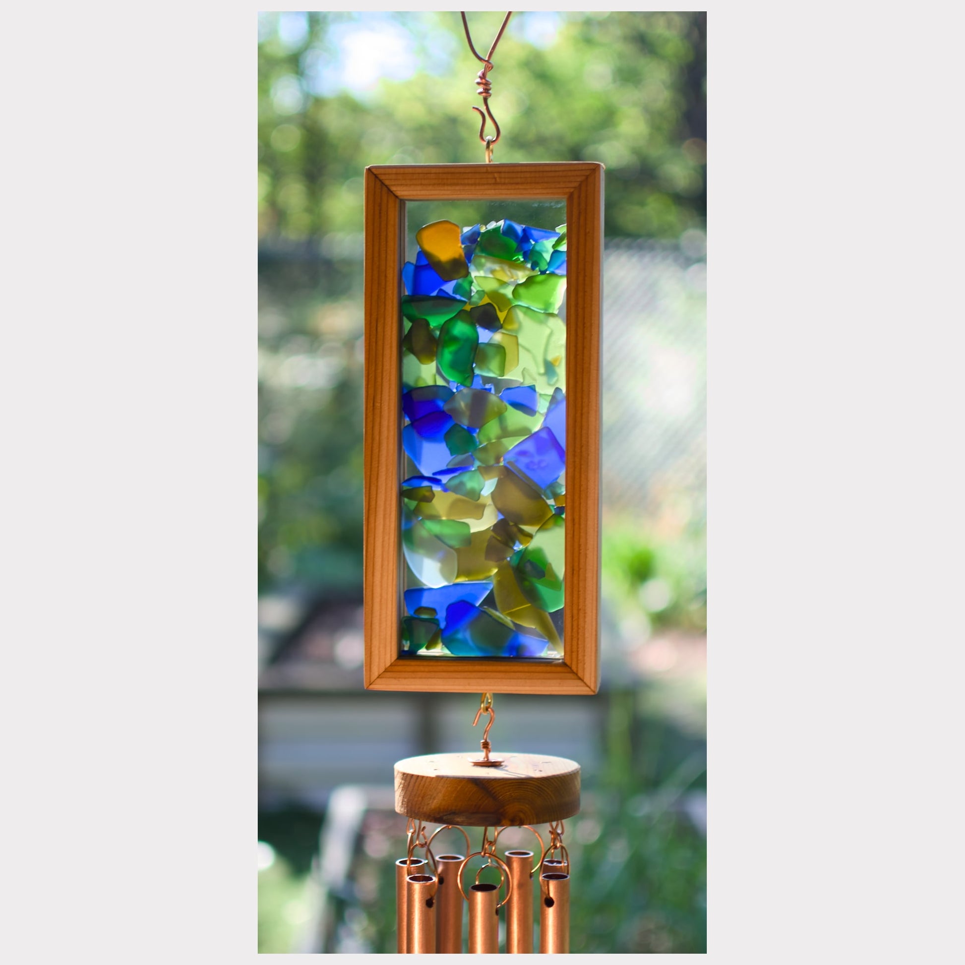 Decorative wind chime with colorful glass panels and wooden frame against a blurred green outdoor background.