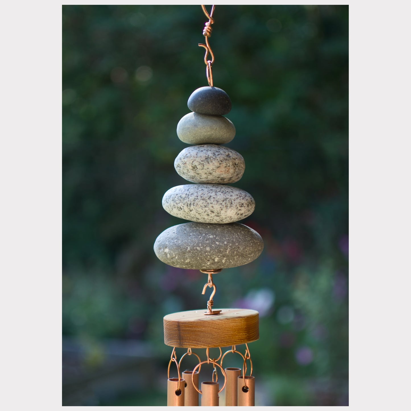 Stacked stone wind chime with wooden base against a blurred natural background