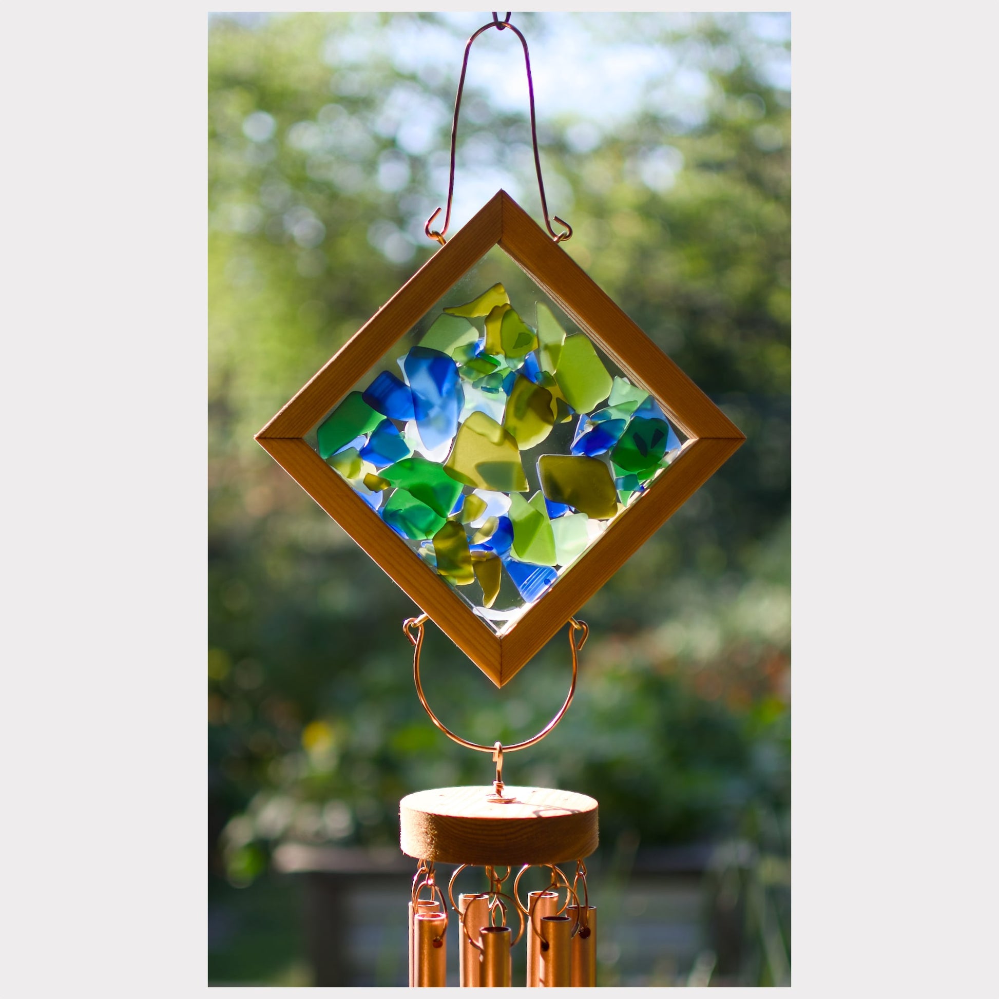 Decorative glass wind chime with colorful glass pieces and a wooden base against a blurred green background.