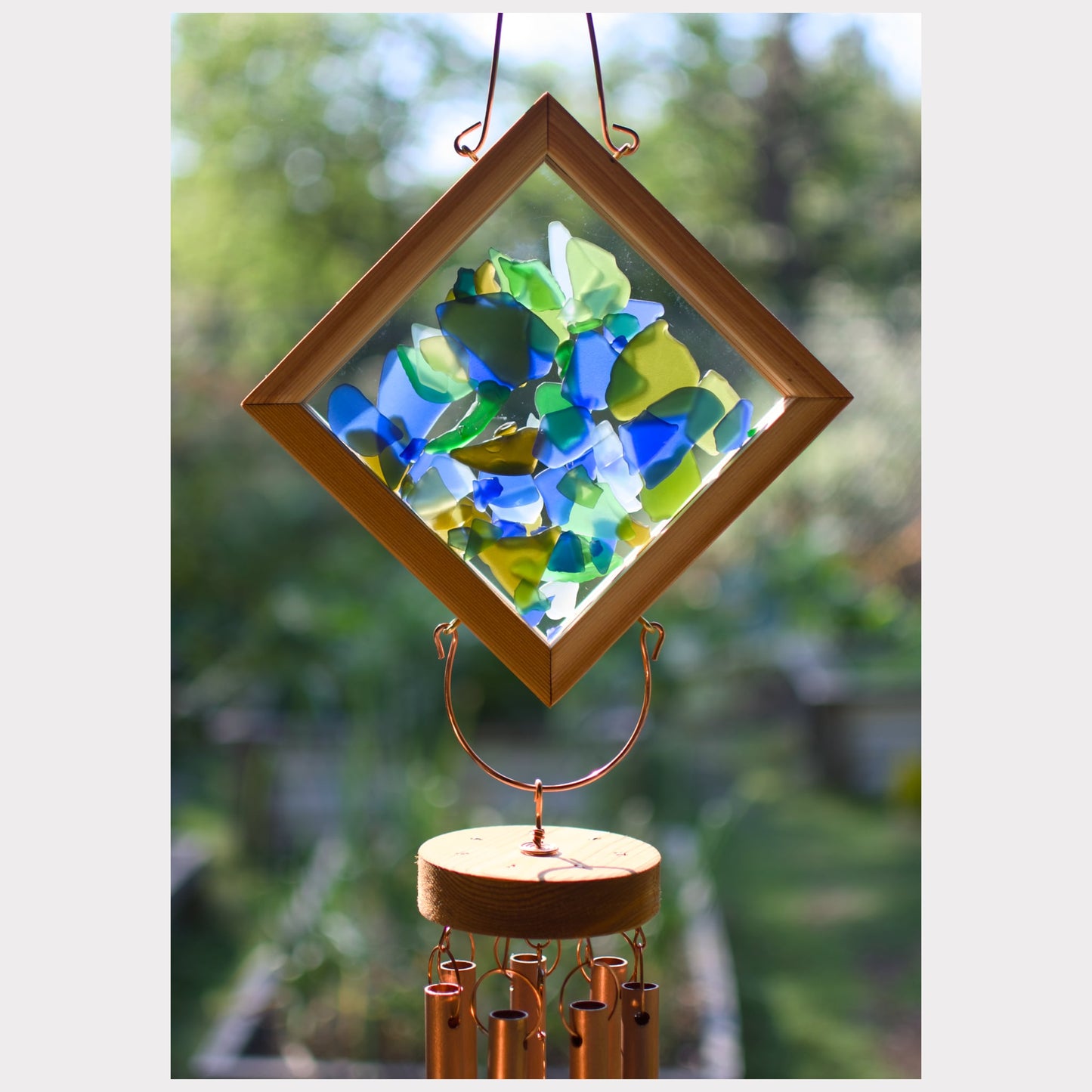 Decorative wind chime with stained glass panel and wooden base against a blurred green background