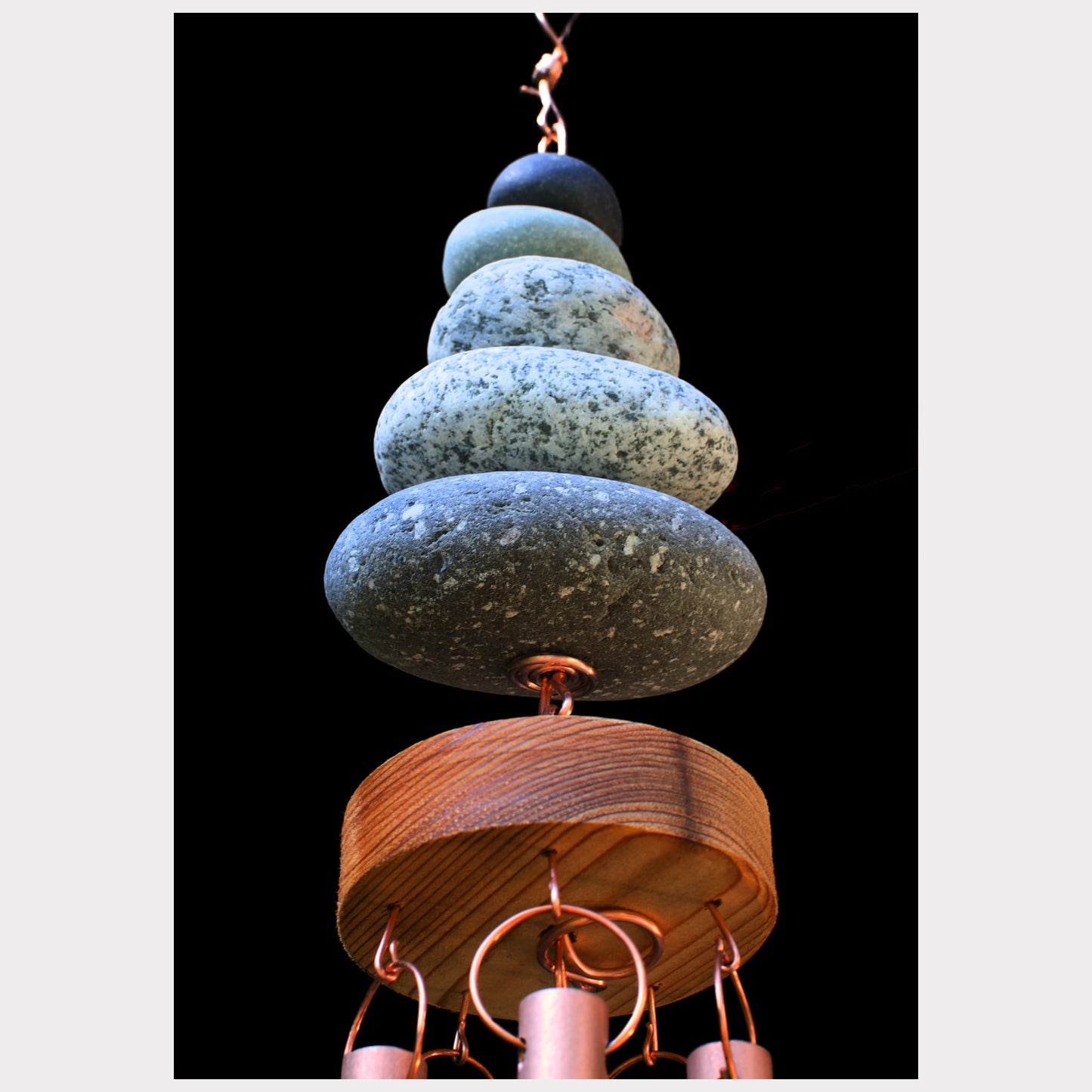 Decorative hanging sculpture with stacked stones and wooden base on a black background