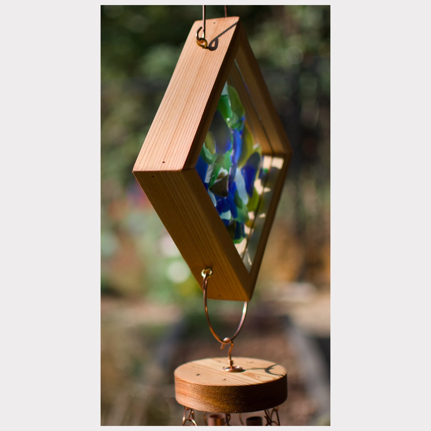 Wooden wind chime with colorful glass panels against a blurred natural background