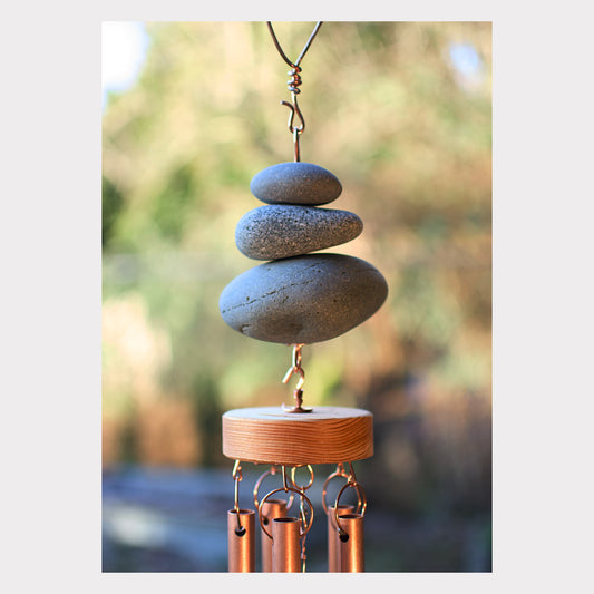 Decorative wind chime with stacked stones and copper tubes against a blurred natural background