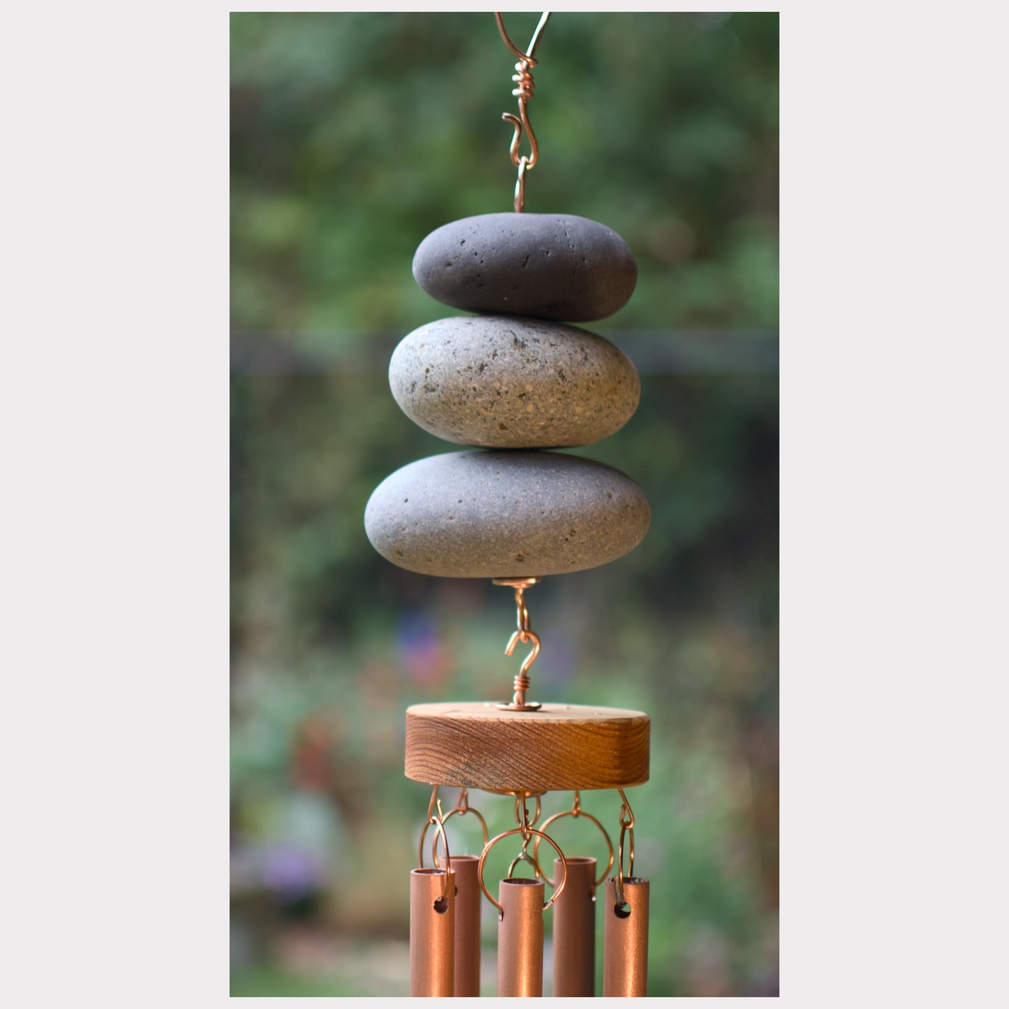 Decorative wind chime with stacked stones and copper tubes against a blurred natural background
