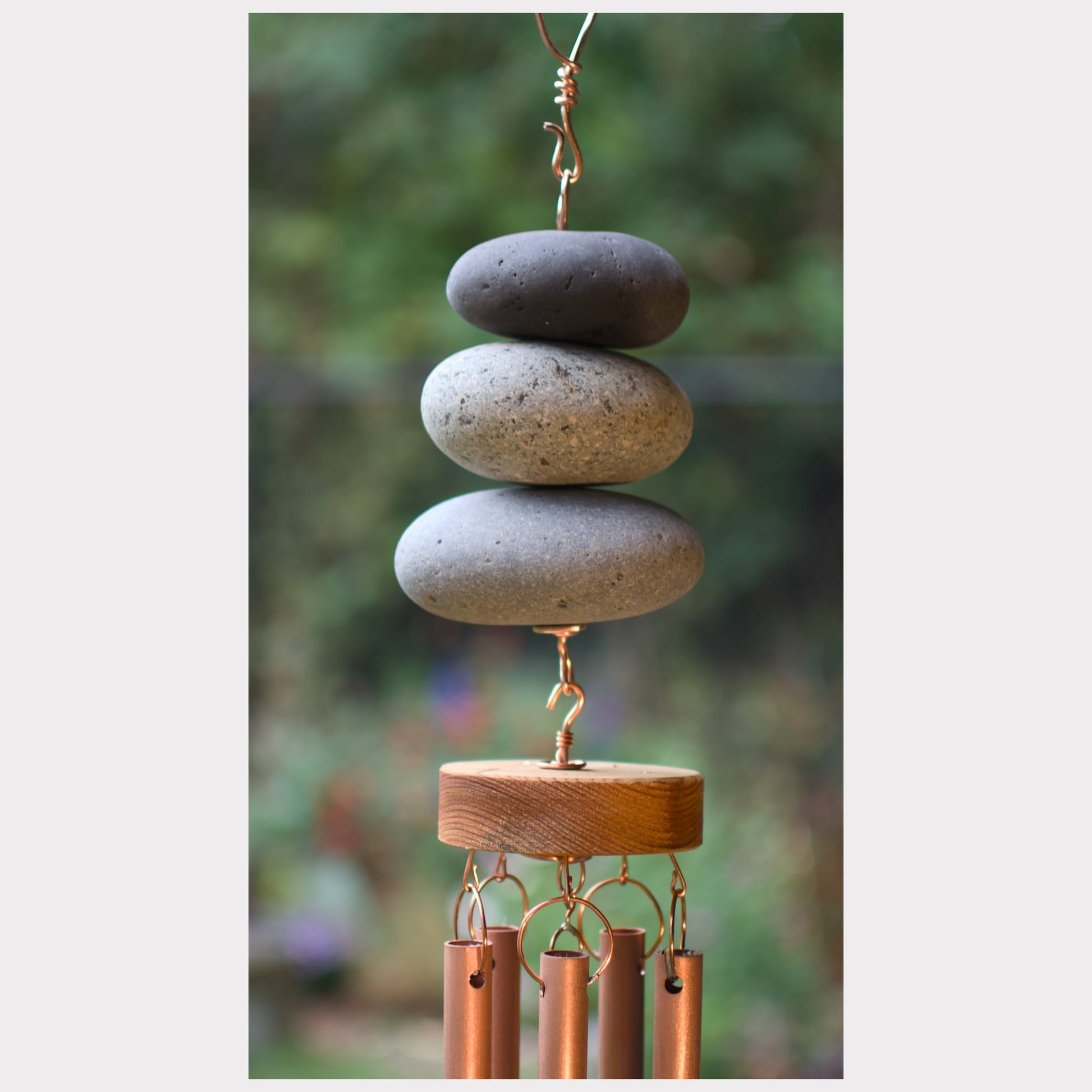 Decorative wind chime with stacked stones and copper tubes against a blurred natural background