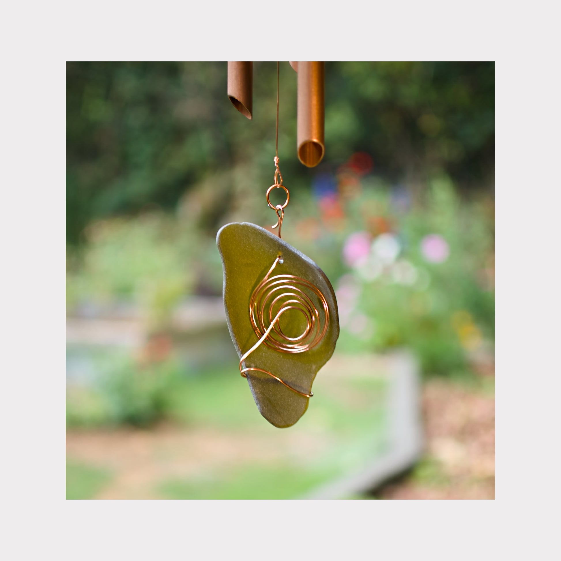 Decorative wind chime with an artist-made copper wrapped beach glass windsail against a blurred garden background.
