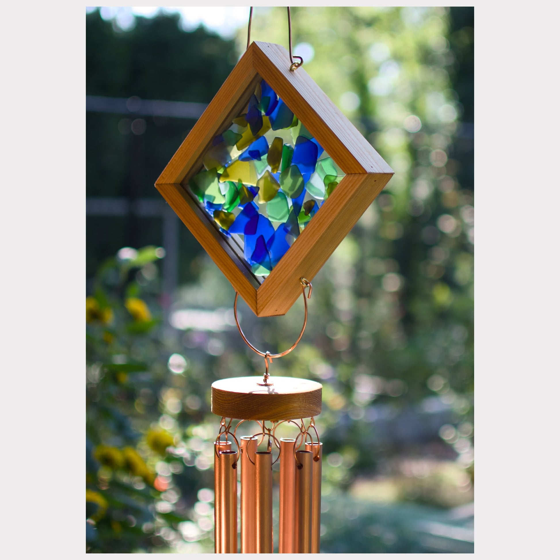 Decorative wind chime with stained glass panel and copper tubes against a blurred natural background
