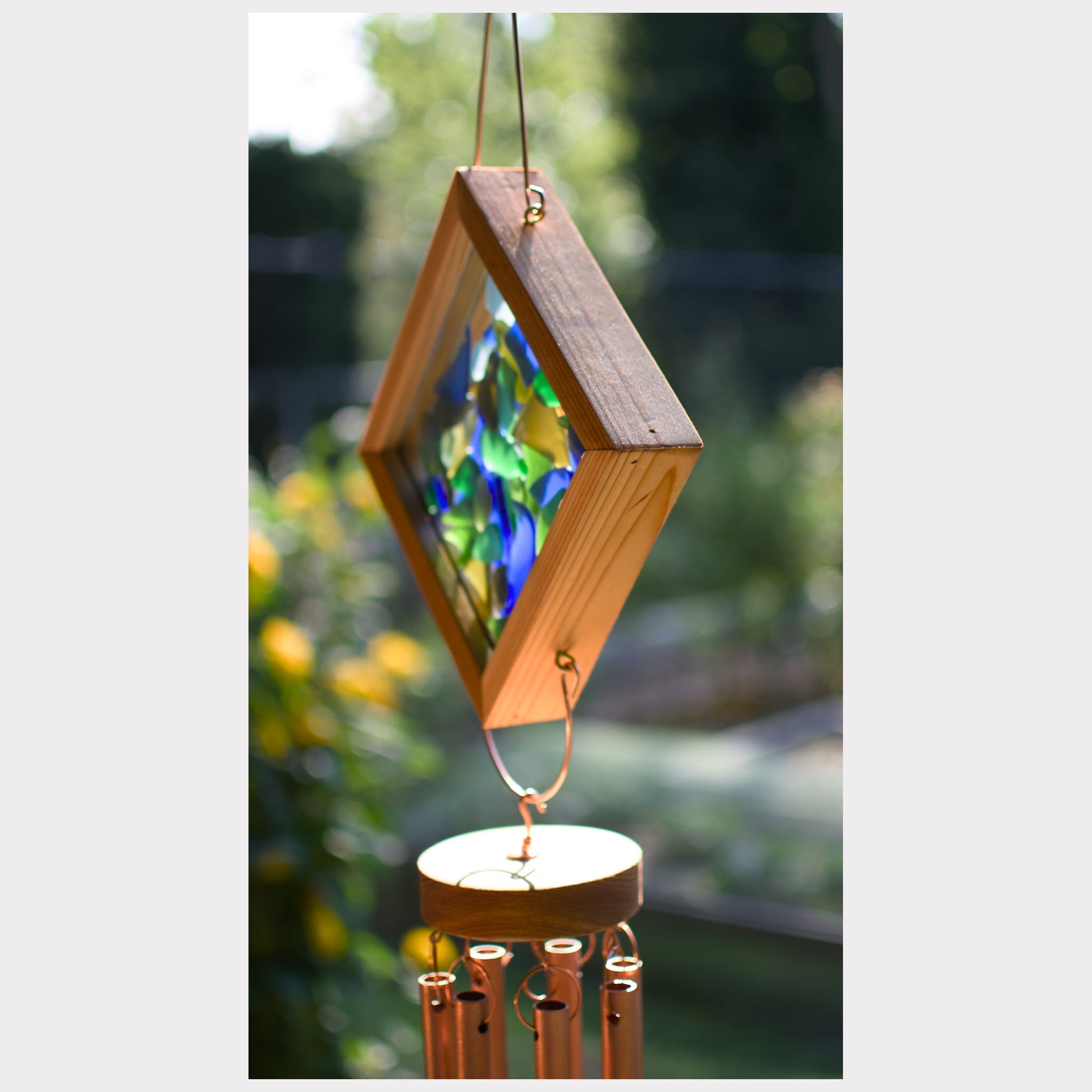 Wooden wind chime with stained glass panel against a blurred garden background