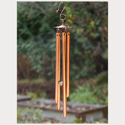 Copper wind chime with blurred greenery in the background