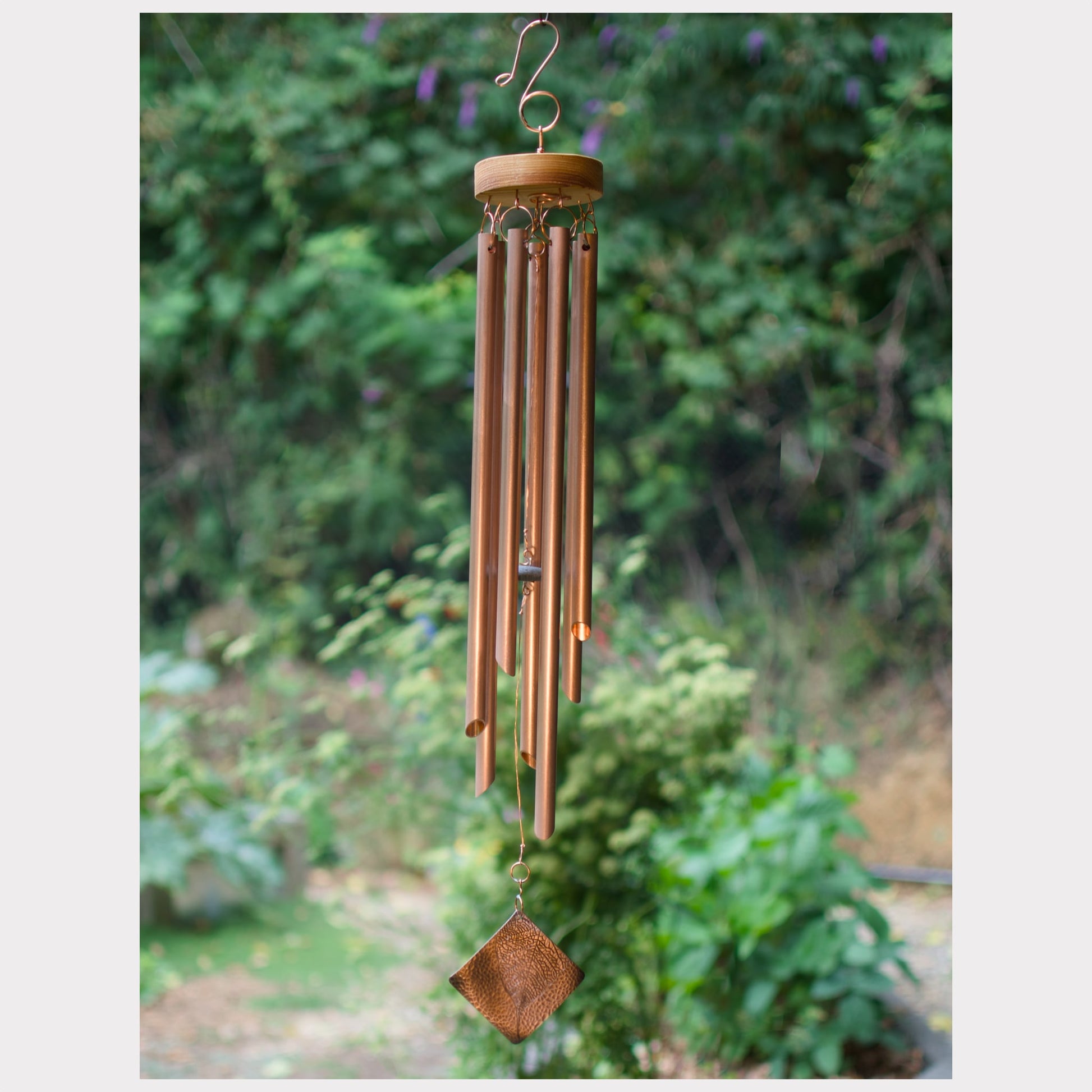 Copper wind chime with a blurred green garden background, and a leaf imprint windsail.