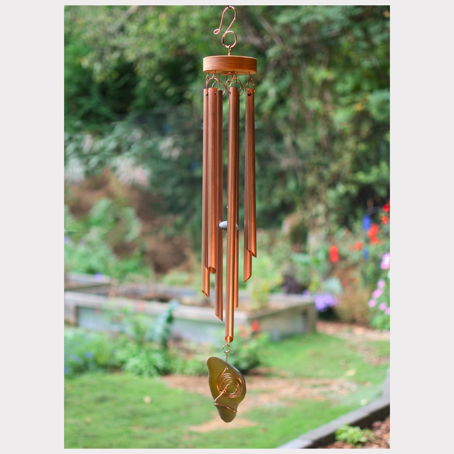 Copper wind chime hanging in a garden with greenery in the background