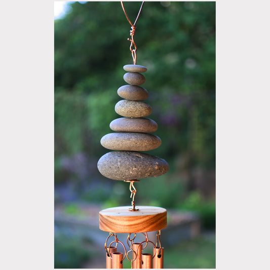 Stacked stone wind chime with wooden base against a blurred natural background