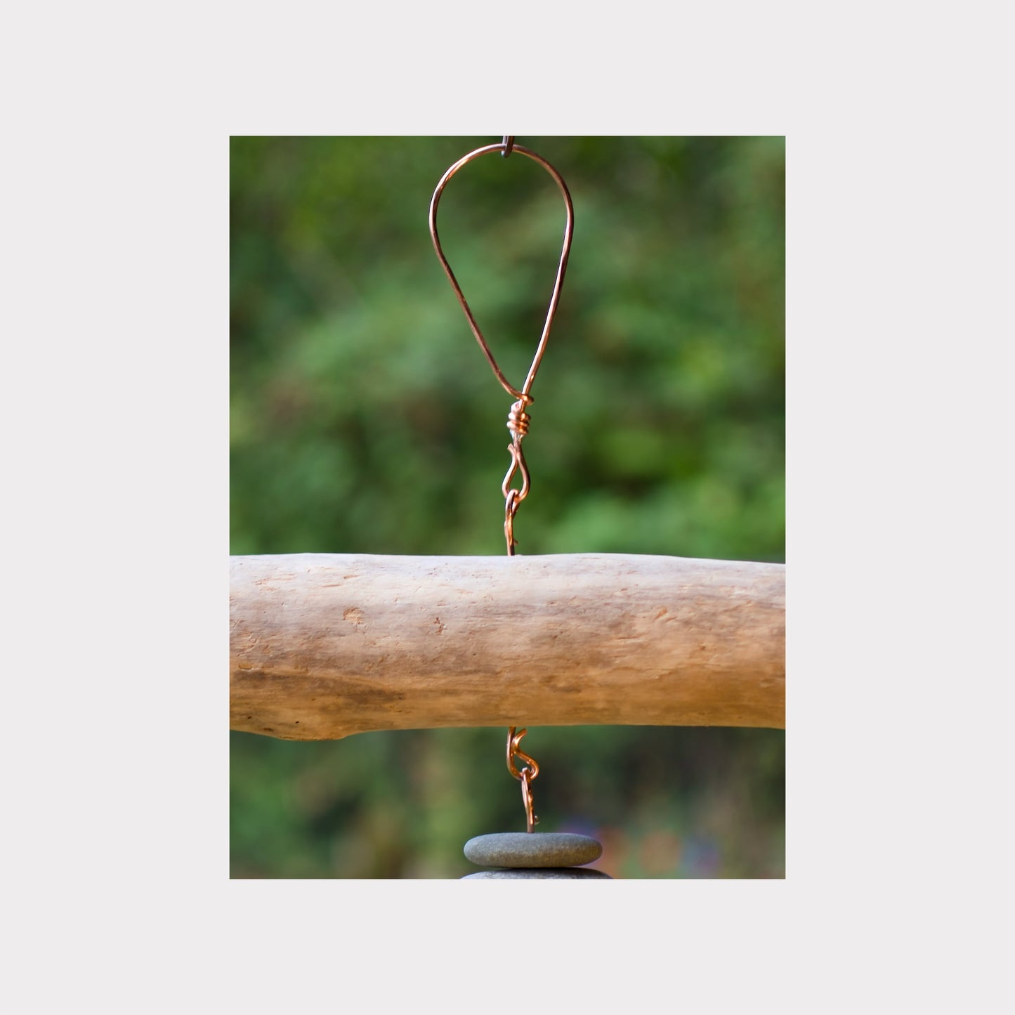 Copper hook with a stone on a wooden log against a blurred natural background