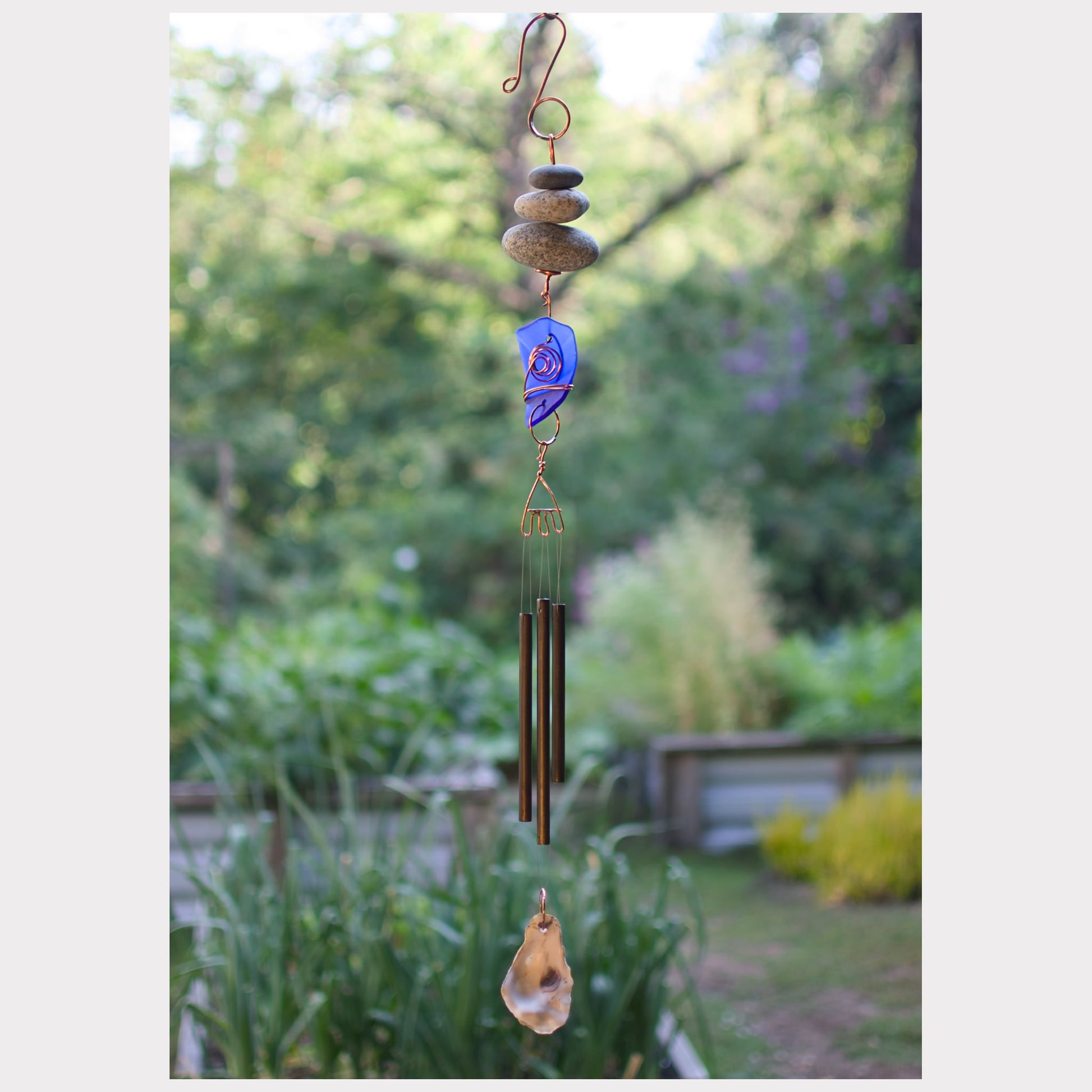 Zen wind chime featuring three natural beach stones, cobalt blue glass, three handmade brass chimes, and an oyster half shell windsail.