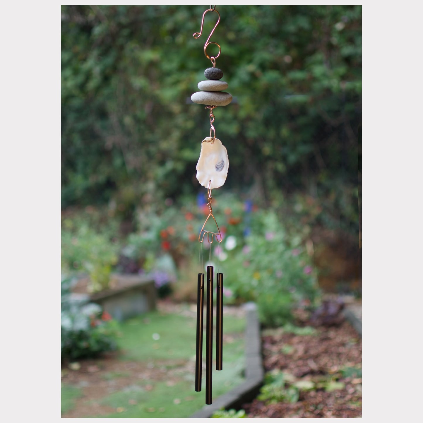 Decorative wind chime with stones and metal tubes in a garden setting