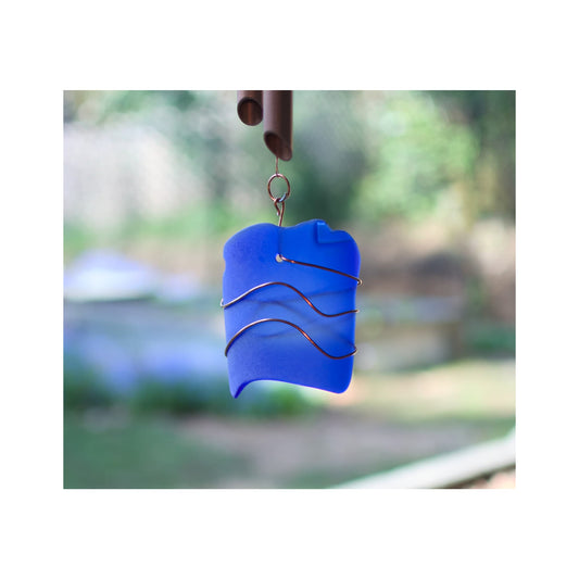 Blue glass wind chime with wavy design against a blurred outdoor background