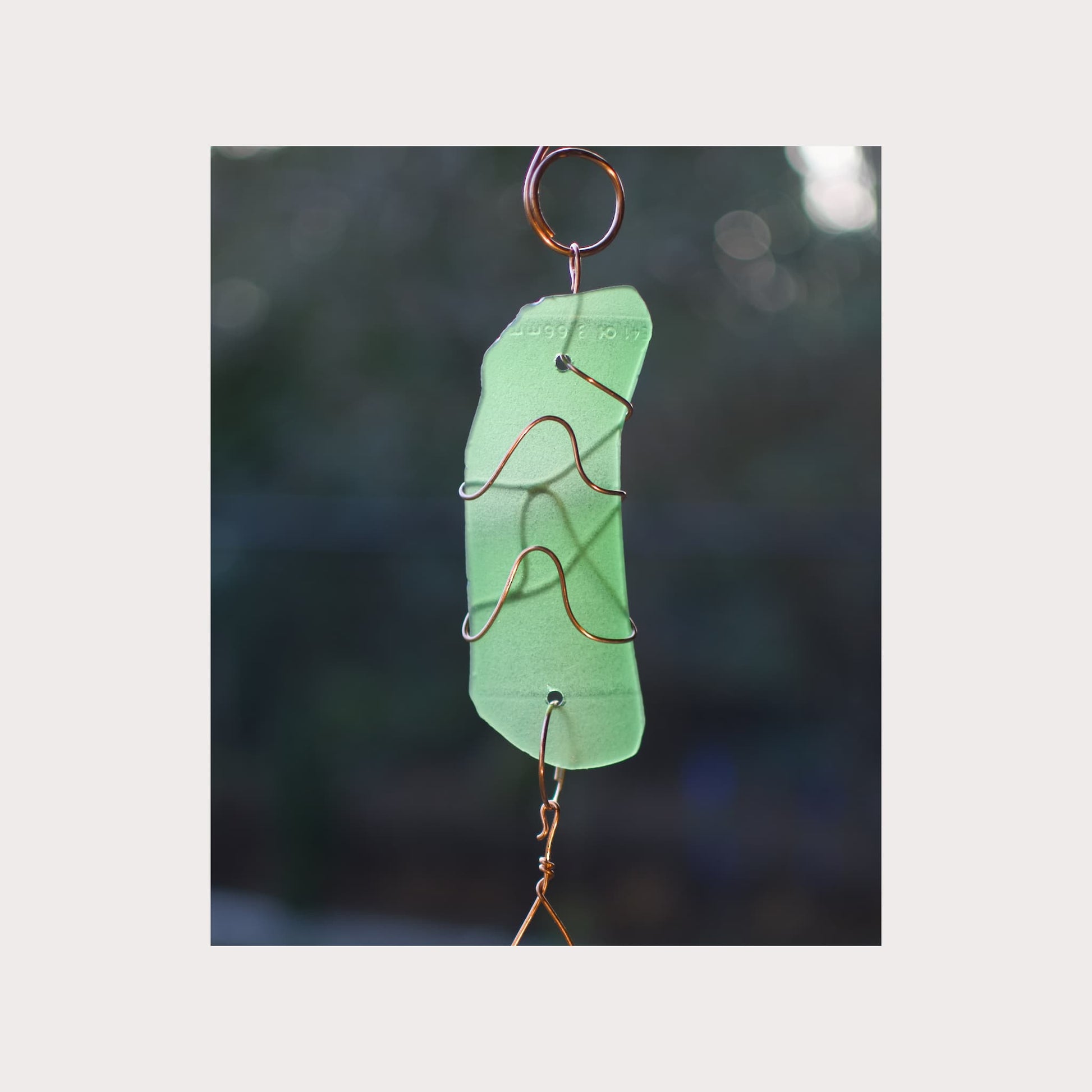 Green glass ornament with copper wire on a blurred natural background