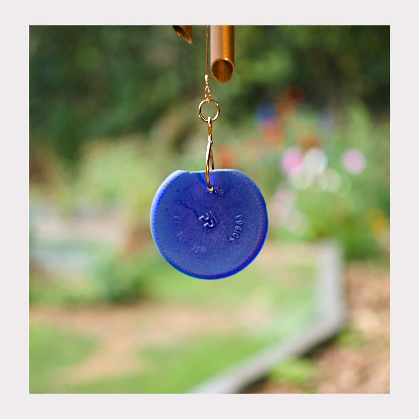 Blue wind chime disc with a blurred garden background