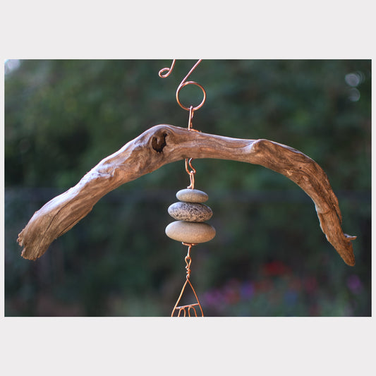Driftwood wind chime with stacked stones against a blurred natural background