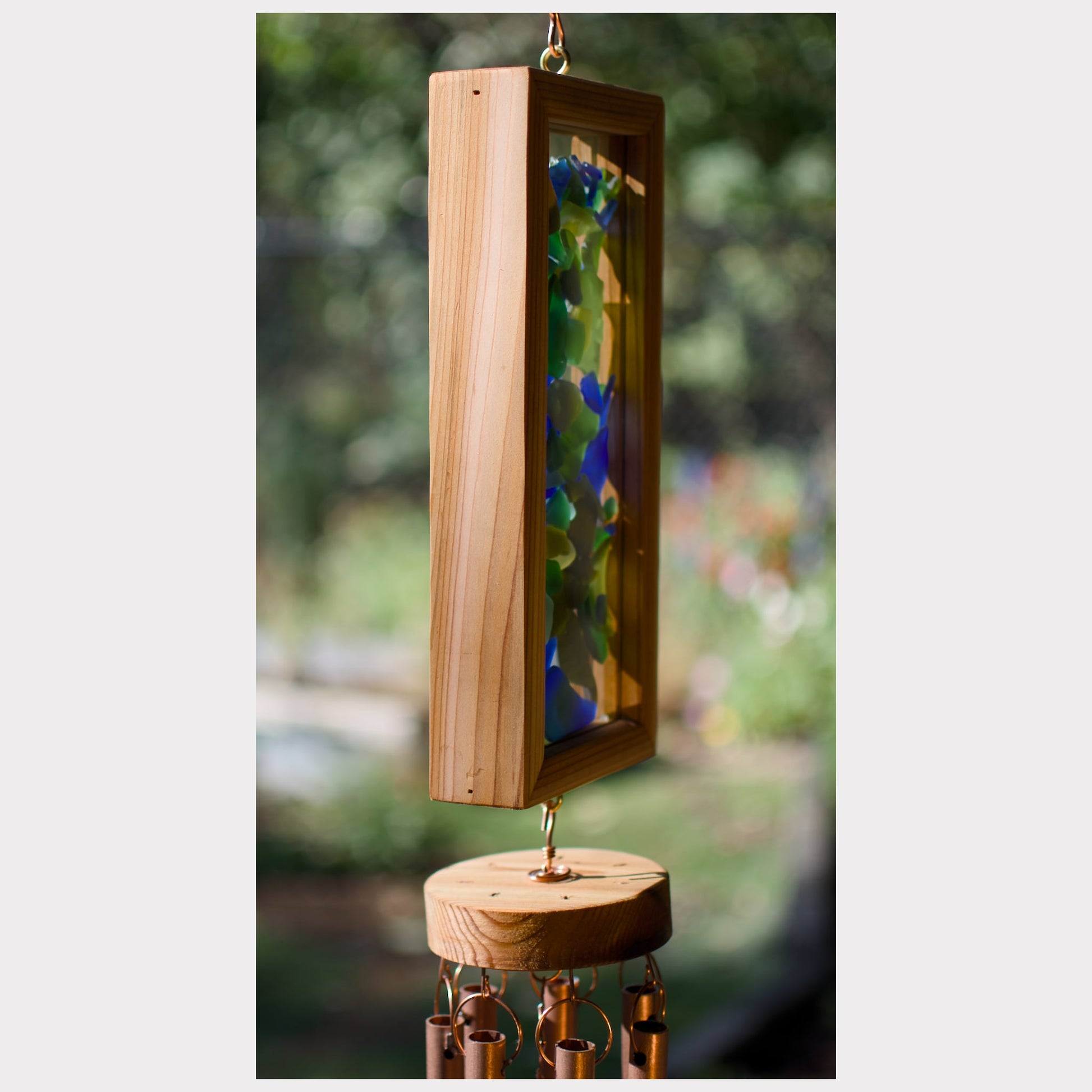 Wooden wind chime with colorful glass elements against a blurred natural background