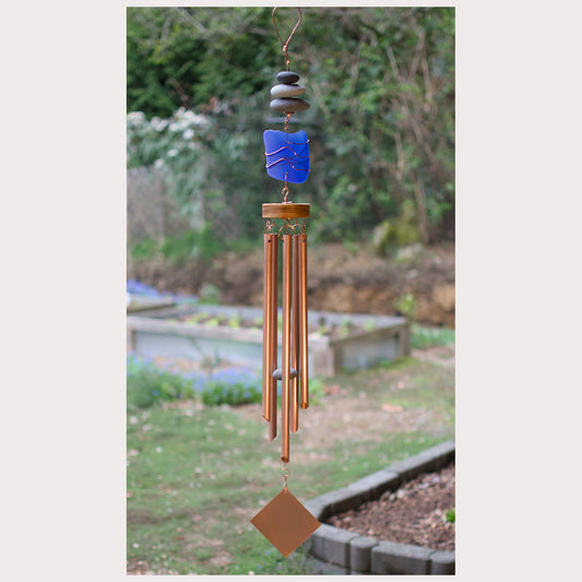 Decorative wind chime with blue sea glass and copper tubes against a garden background