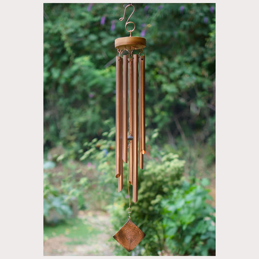 Copper wind chime with greenery in the background