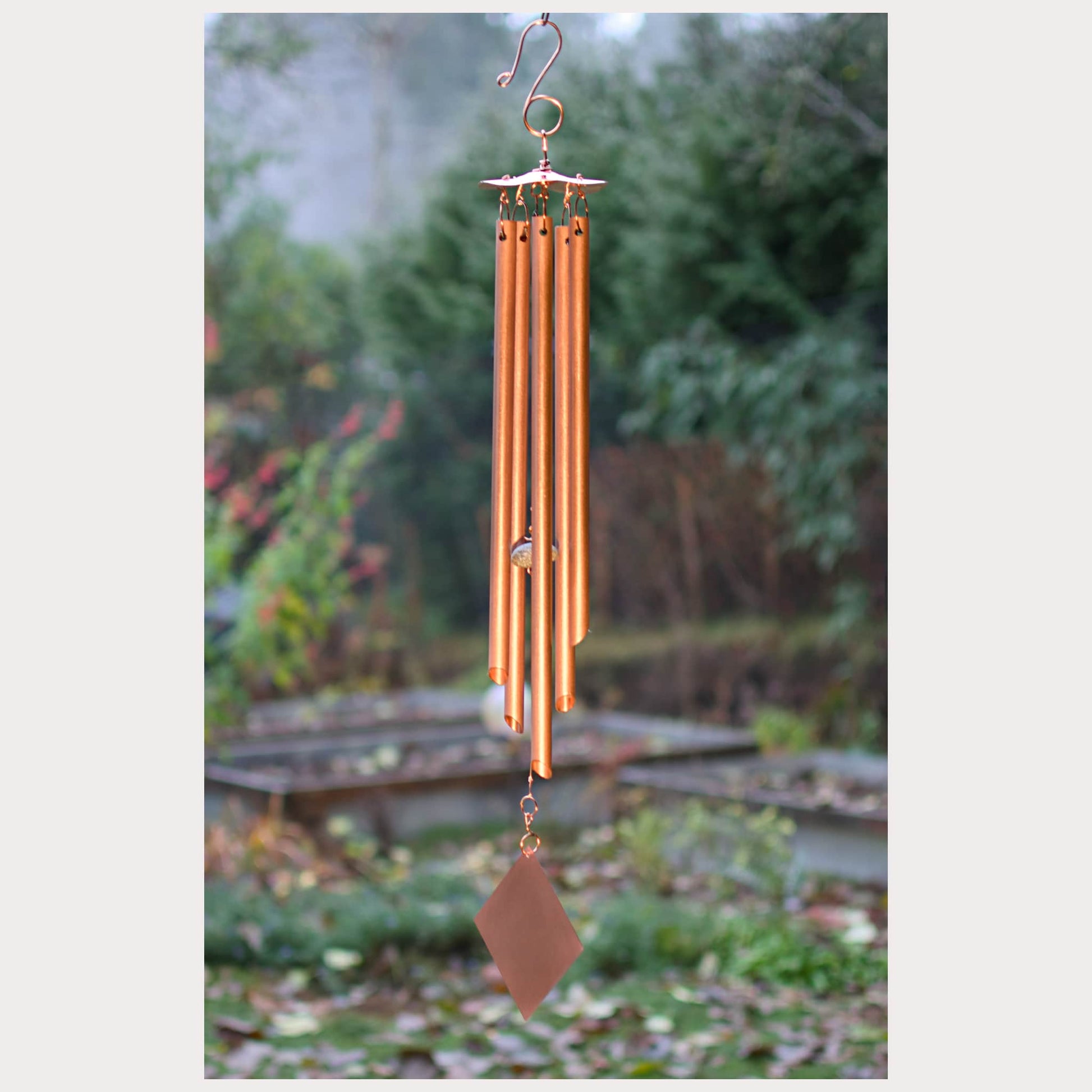 Copper wind chime hanging in a garden with blurred greenery in the background