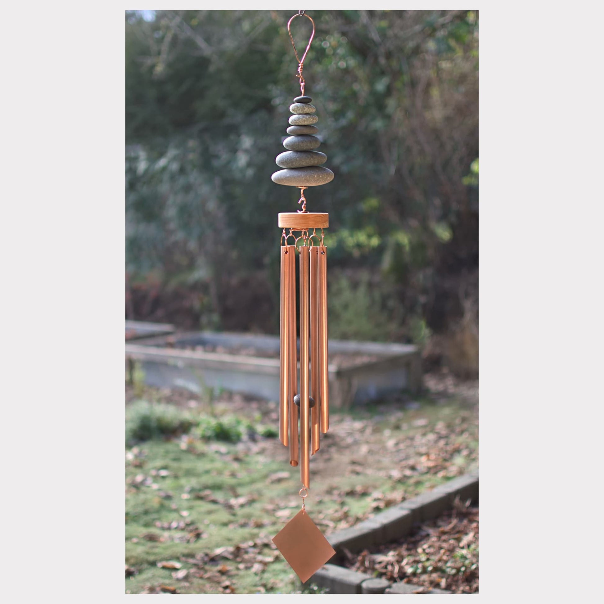 Decorative wind chime with stones and copper elements against a natural background