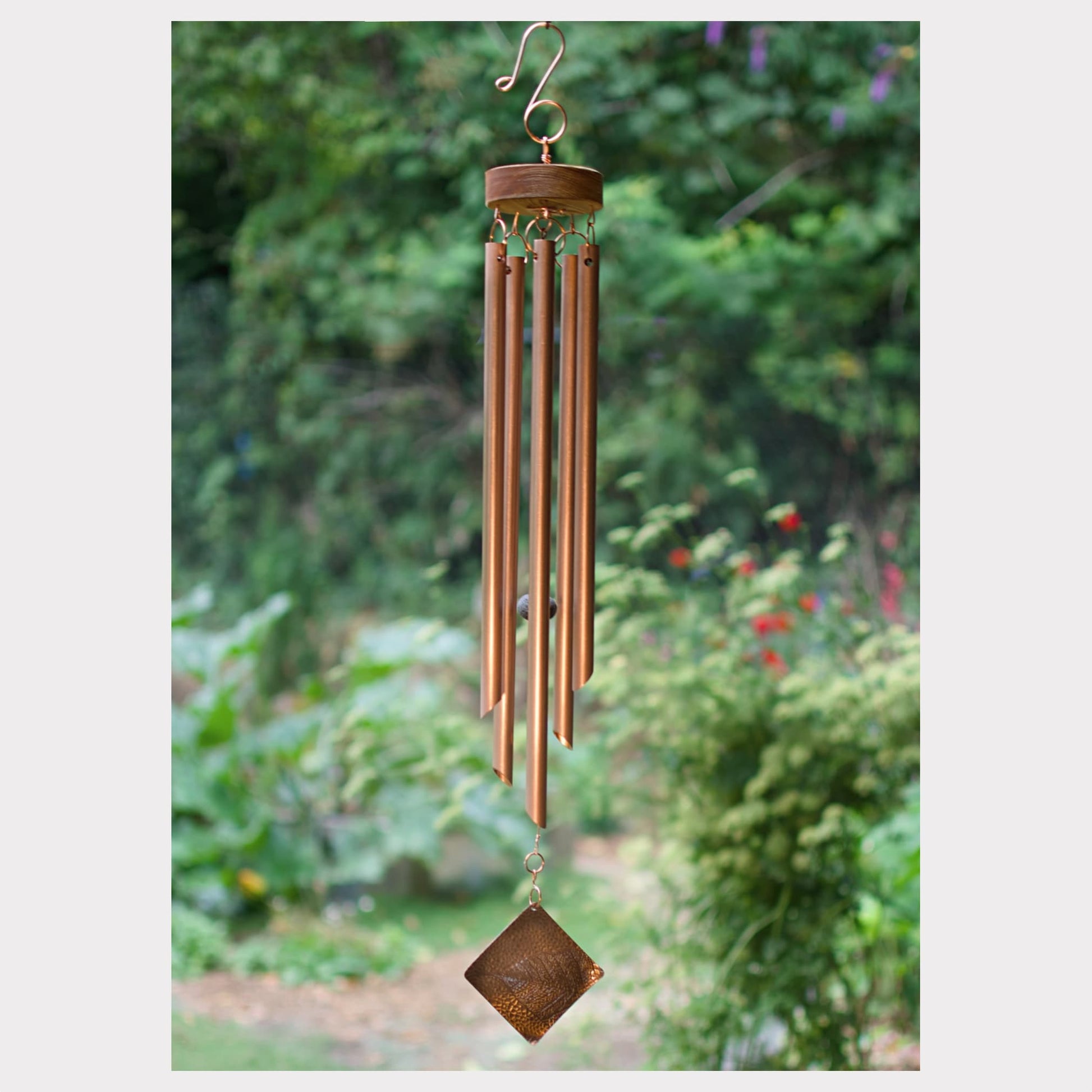 Copper wind chime with decorative elements against a blurred garden background