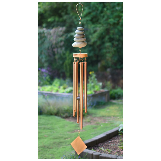 Decorative wind chime with stones and copper tubes against a garden background