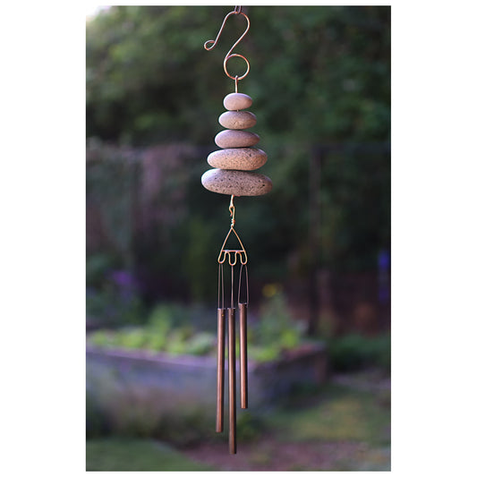 Decorative wind chime with stacked stones and brass tubes against a garden background