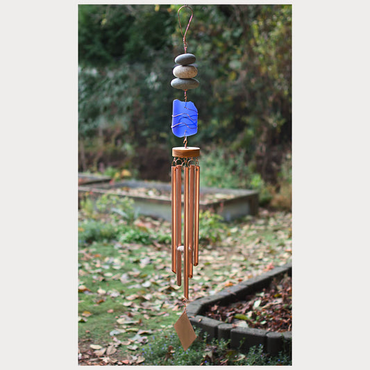 Decorative wind chime with blue glass piece and pebbles in a garden setting