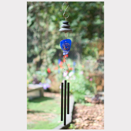 Decorative wind chime with blue glass piece and green metal tubes against a garden background