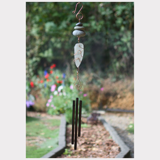 Decorative wind chime with pebbles and a feather-like design in a garden setting.