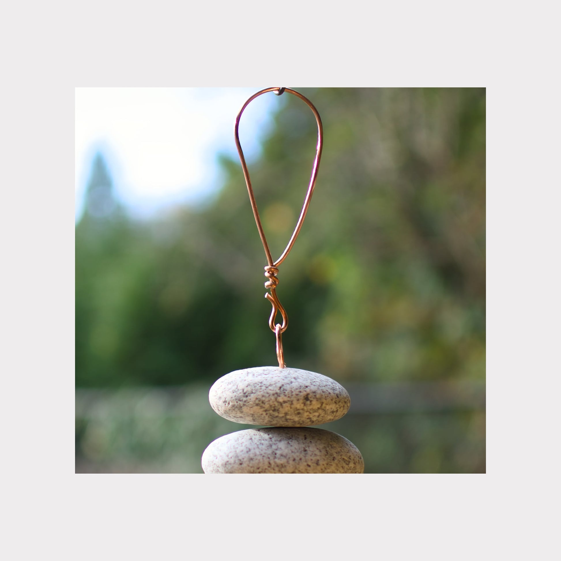 Copper hook with stones stacked below against a blurred natural background
