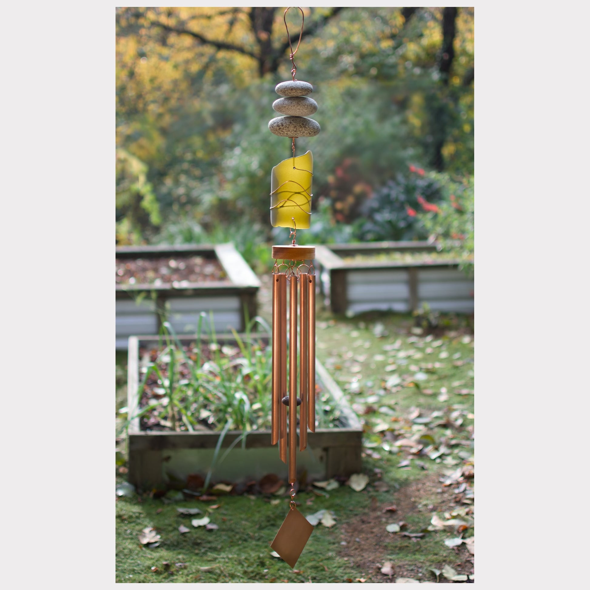 Decorative wind chime in a garden setting with trees and plants in the background.