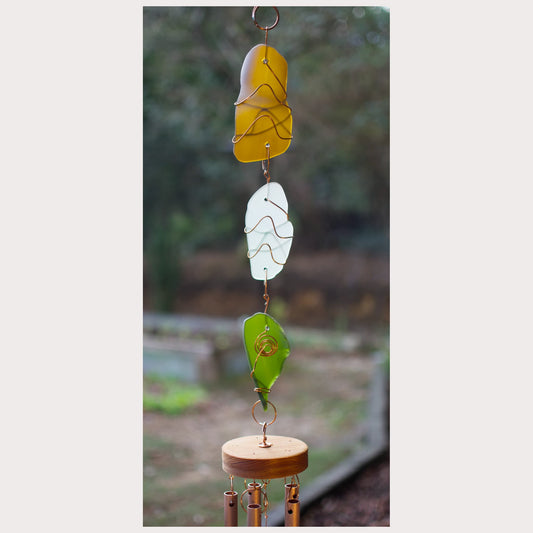 Decorative wind chime with glass panels and wooden base against a blurred natural background
