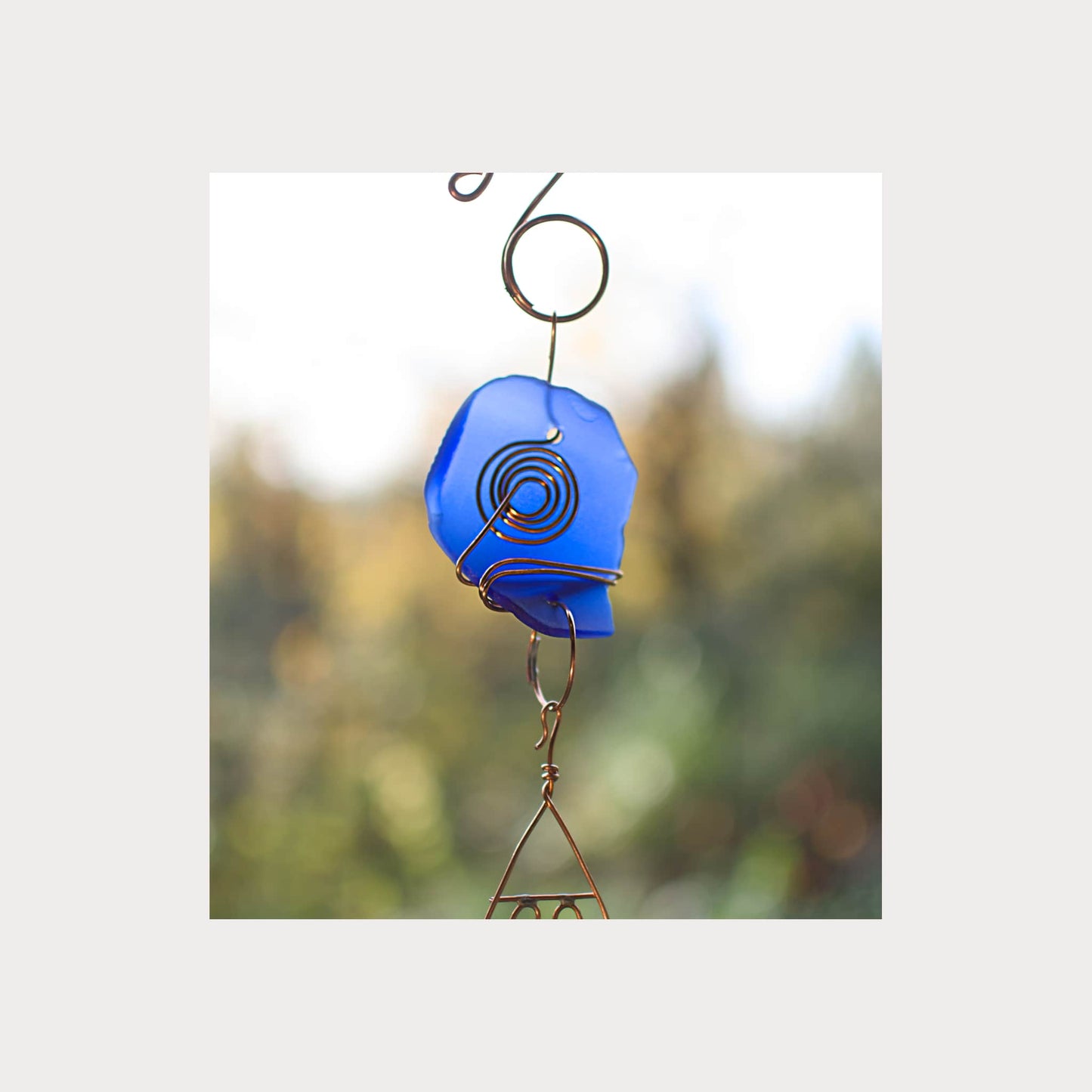 Blue glass wind chime with spiral design against a blurred green background