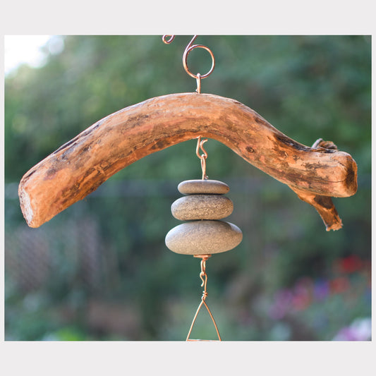 Driftwood and stone wind chime against a blurred natural background