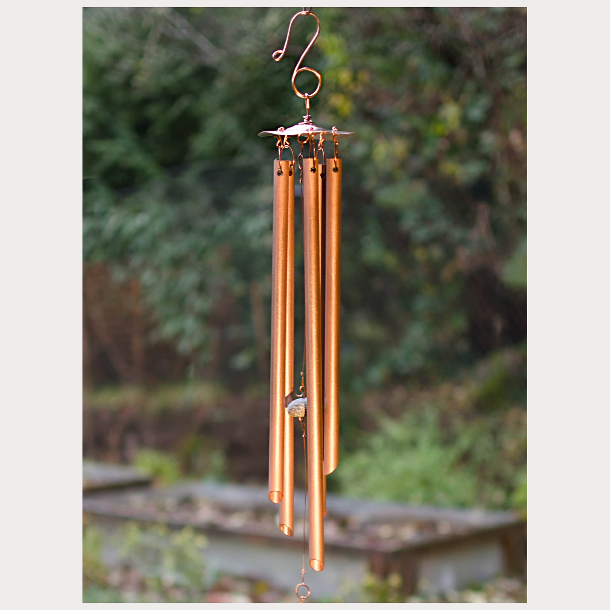 Copper wind chime with blurred greenery in the background