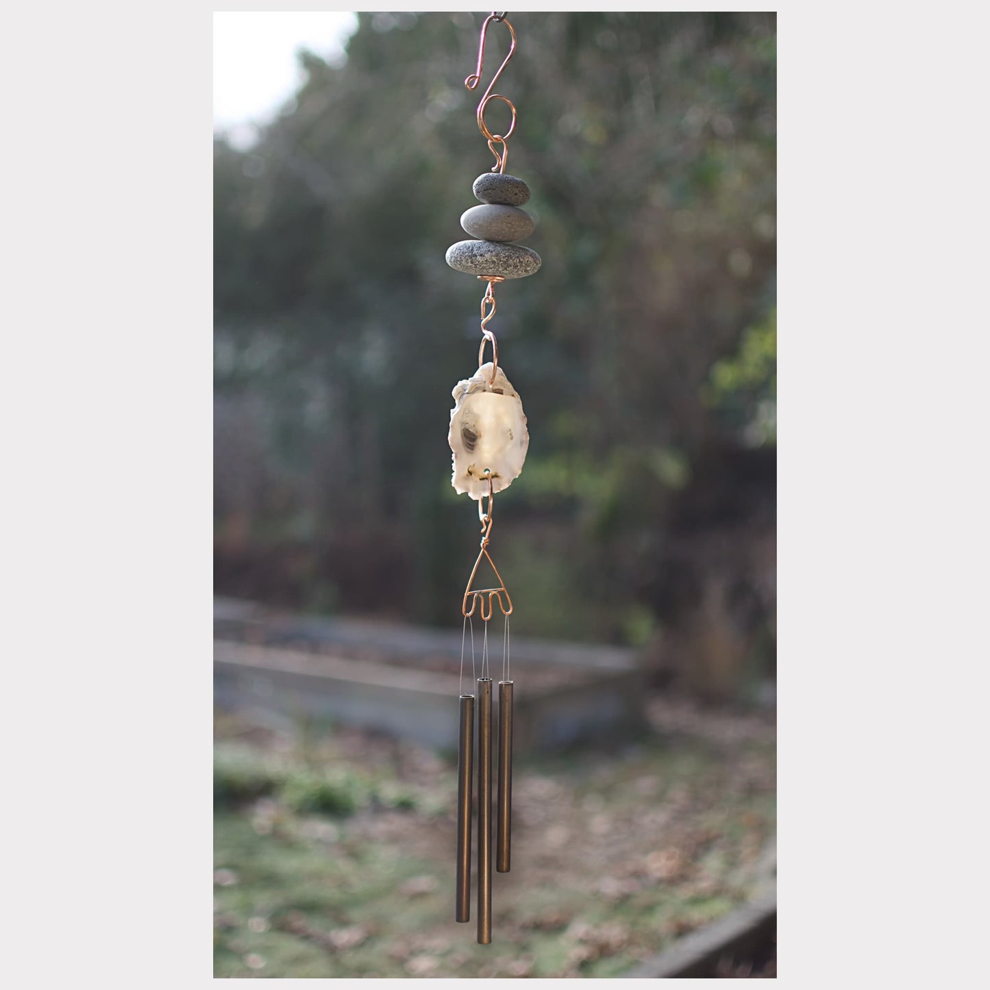 Decorative wind chime with stones and metal tubes against a natural background