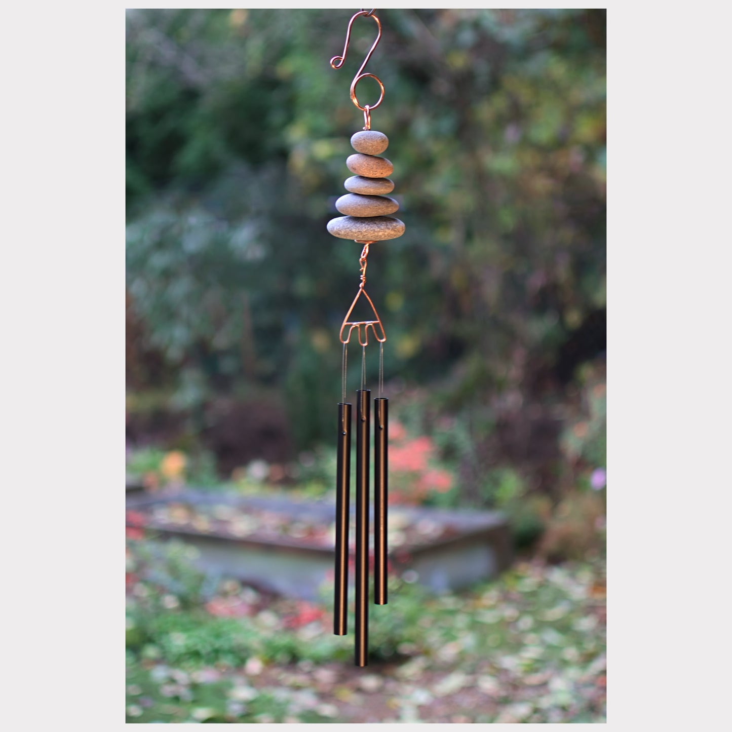Decorative wind chime with stones and metal tubes against a garden background