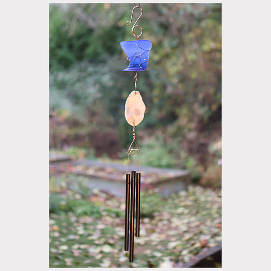 Decorative wind chime with blue and beige elements against a garden background