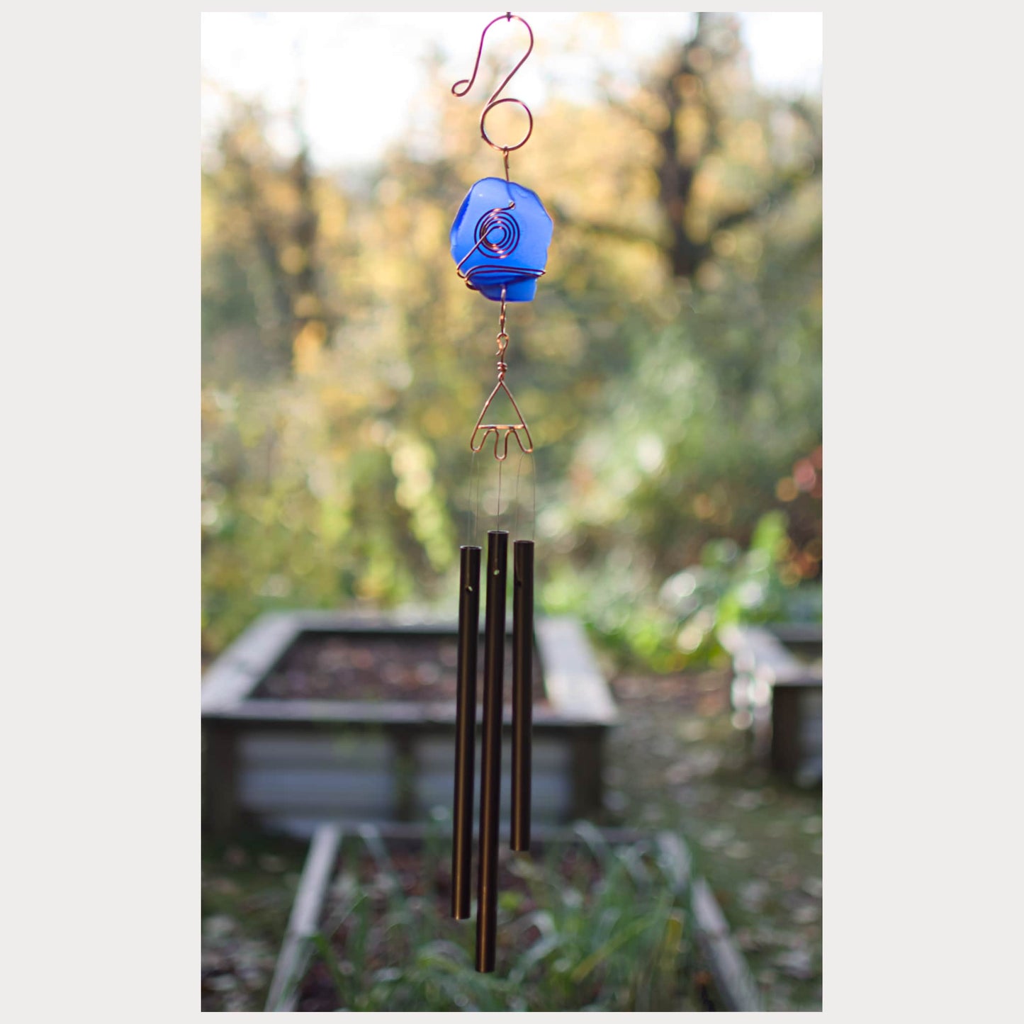 Decorative wind chime with a blue hanging element in a garden setting