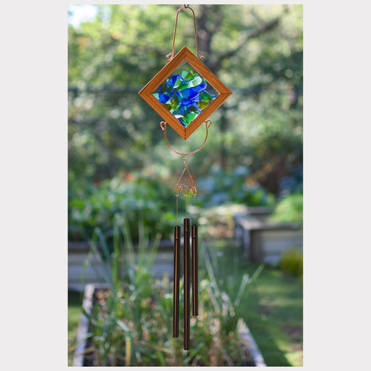 Decorative wind chime with colorful glass panel and metal tubes against a garden background