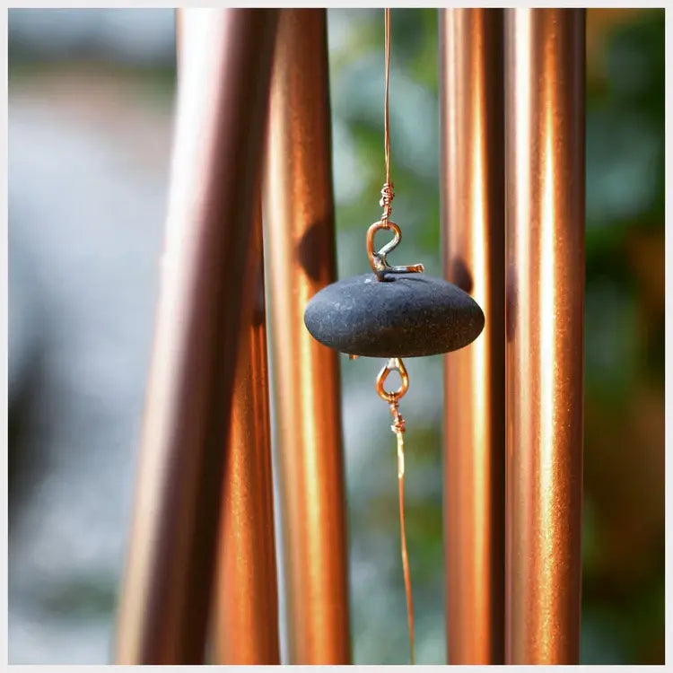 Copper wind chime with a stone weight against a blurred natural background