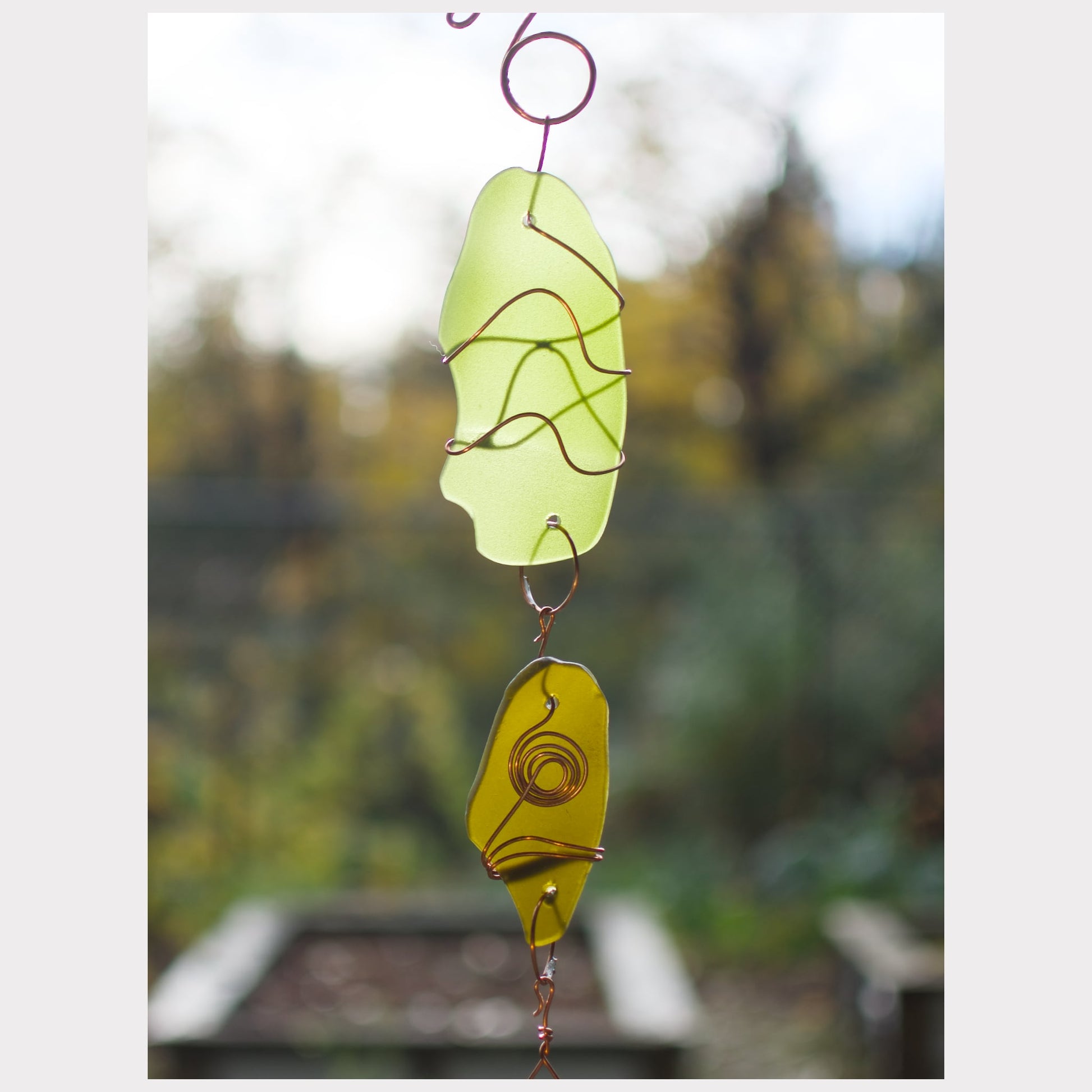 Decorative glass hanging with green and yellow colors against a blurred natural background